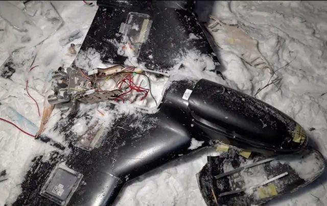 Ушкоджений чорний безпілотник у снігу.