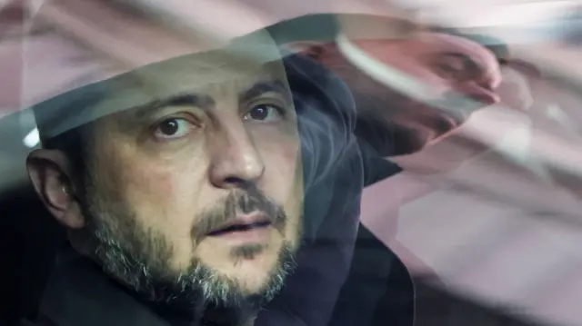 ፕረዚደንት ዩክረይን ቮሎድሚር ዘለንስኪ ኣብ ውሽጢ ኮፍ ኢሉ ከሎ ነጸብራቕ ናይ ሓደ ሓላፊ ጸጥታ ኣብ መስኮት መኪና ይርአ።