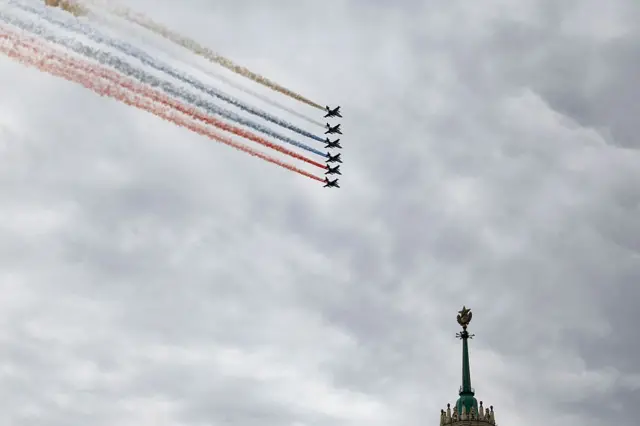 Aviones de combate rusos lanzan humo con los colores de la bandera rusa mientras sobrevuelan el centro de Moscú; en la imagen se aprecia la parte superior de la cúpula de un edificio.
