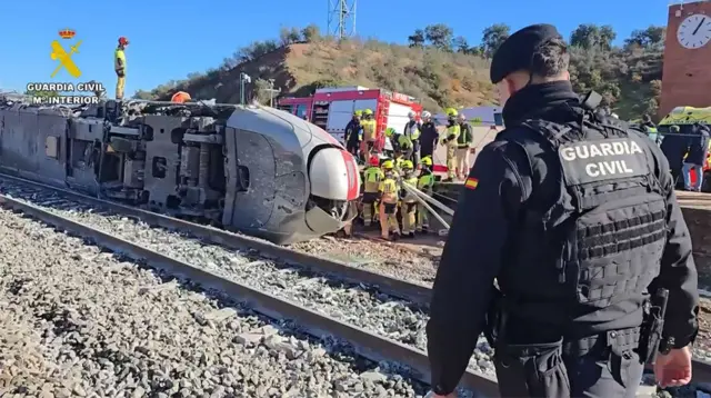 Un agente de la Guardia Civil española vestido en uniforme negro observa a una decena de rescatistas cerca de un tren volcado 