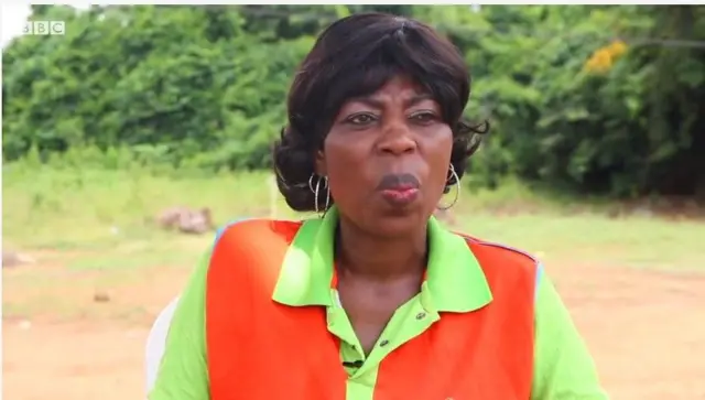 Queen Abosede, olutọju awọn opo wọ T-shirt alawọ eweko ati ọsan, o de irun atọwọda sori