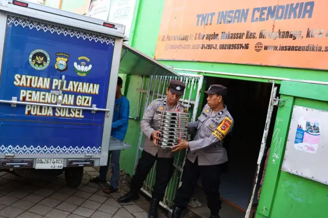 Dua polisi sedang membawa rantang makanan untuk MBG.
