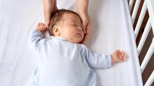 Mãos seguram a cabeça de um bebê dormindo no berço.