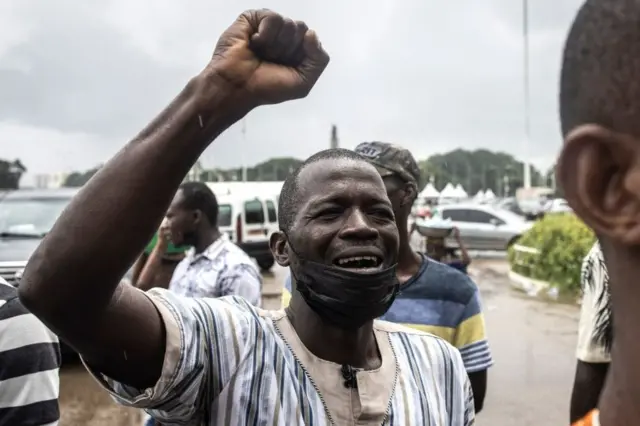 Un membre de la société civile guinéenne chante l'hymne national devant le Palais du peuple.