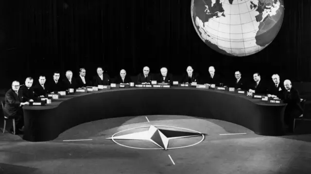 Delegaci siedzą przy półokrągłym stole na konferencji NATO w Paryżu. Czarno-biała fotografia.