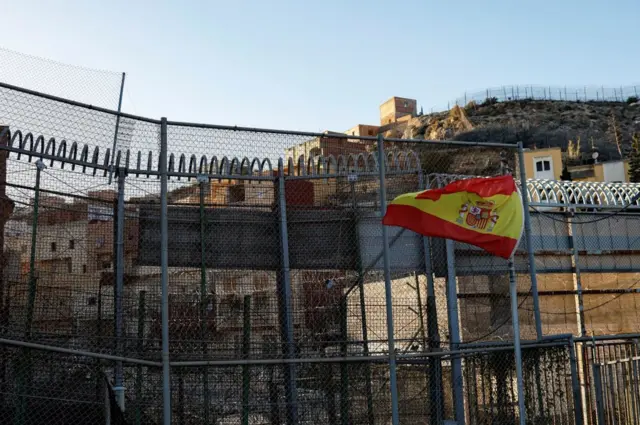 Esta fotografía, tomada el 24 de febrero de 2024 en Melilla, muestra una bandera de España en una valla cerca de un paso fronterizo cerrado entre Marruecos (arriba) y el enclave español de Melilla, en el norte de África.