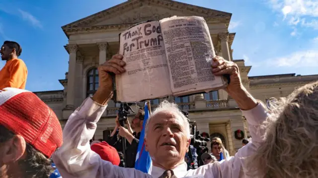 Um manifestante segurando uma Bíblia que diz "Graças a Deus por Trump", fora do Capitólio do Estado da Geórgia, em novembro de 2020

