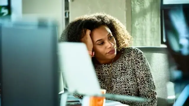 Uma mulher negra em frente a um computador olhando para o lado