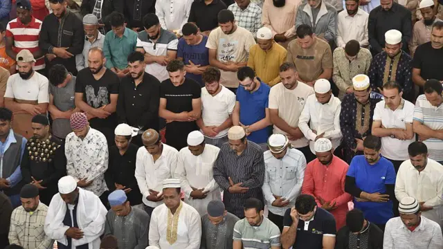 Group of Muslims wey stand as dem dey offer prayer. Dem wear different colour of clothes