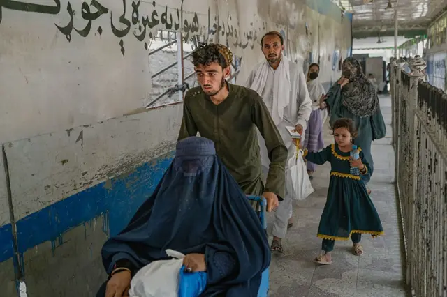 تصویر شماری از مهاجرین را نشان می‌دهد که از طریق گذرگاه تورخم وارد می‌شوند. یک زن روی ویلچیر در تصویر دیده می‌شود.