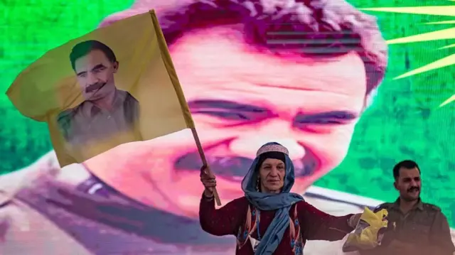 Una mujer ondea una bandera con el rostro de Abdullah Öcalan, frente a una inmensa foto del político kurdo.