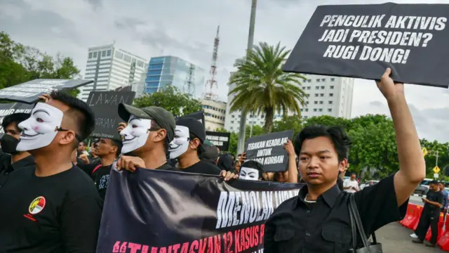 Seorang pendemo yang mengenakan kemeja hitam mengangkat sebuah papan hitam bertuliskan "seret penculik ke penjara, bukan ke istana".