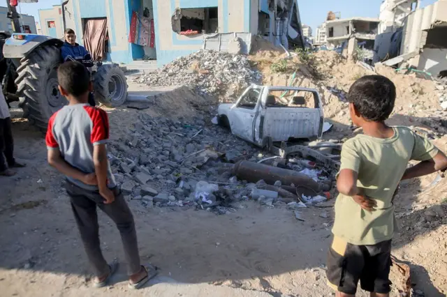 Dos niños caminan junto a un vehículo dañado y bombas sin explotar dentro de un complejo militar de Hamas convertido en refugio en Gaza, el 19 de abril de 2025.