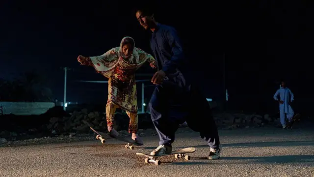 Девушка с покрытой головой и юноша катаются на скейтах