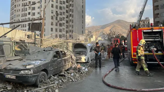 İranda vurulan bir bina ve araçlar itfaiye arabası yanlarında. 