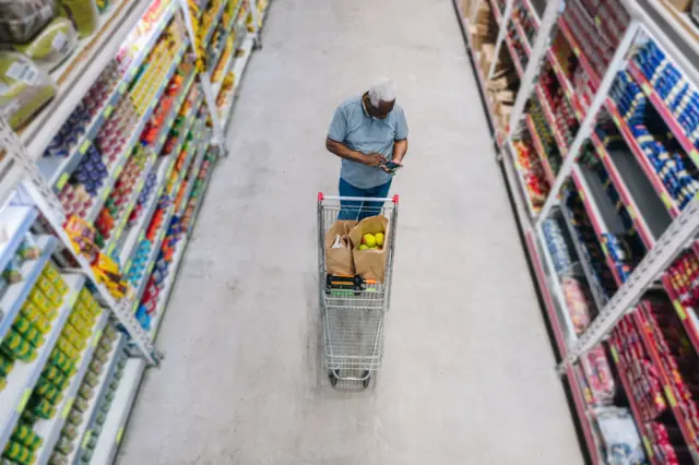 Idoso com carrinho de compras em corredor de supermercado