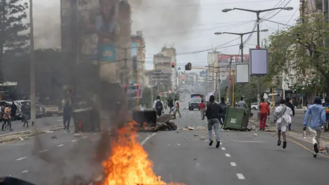 Manifestantes correm na rua, com barricadas 