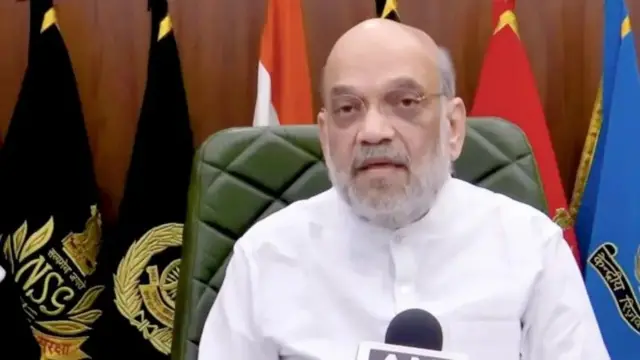 امیت شاه په سپينو کالیو کې ناست دی او مخ کې یې مایکروفون ایښی.