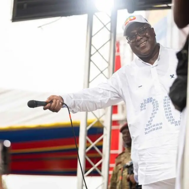 Félix Tshisekedi tendant un micro vers la sourire tout en affichant un sourire