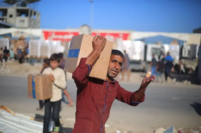 نازحون فلسطينيون يحملون صناديق إمدادات غذائية دخلت غزة بعد استلامها من نقطة توزيع مساعدات في مخيم النصيرات للاجئين وسط قطاع غزة، في 20 أكتوبر/تشرين الأول 2025.