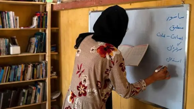 معلمی در کلاس مدرسه مخفی در افغانستان روی تخته‌سفید (وایت‌برد) می‌نویسد