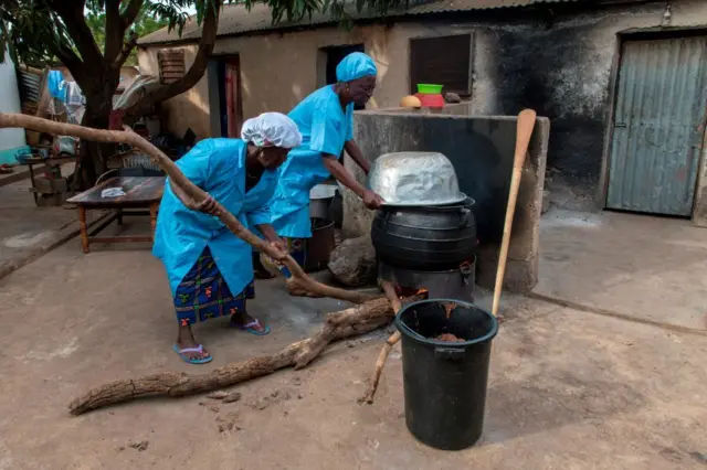 Deux femmes en blouse bleue chauffent une grosse marmite