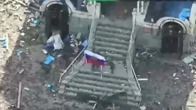 Російський військовий показує прапор РФ на руїнах будинку