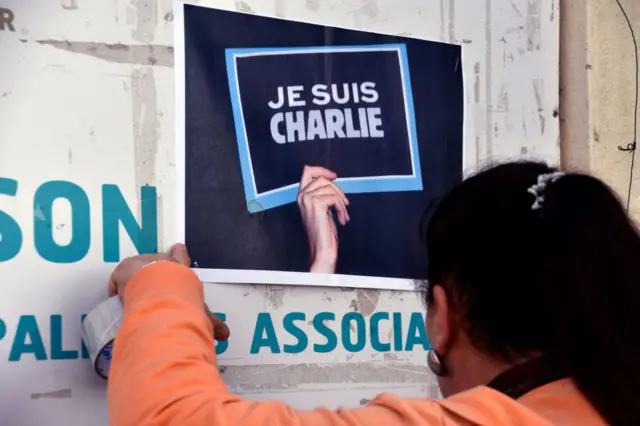 Una mujer pone un poster de "Je suis Charlie"