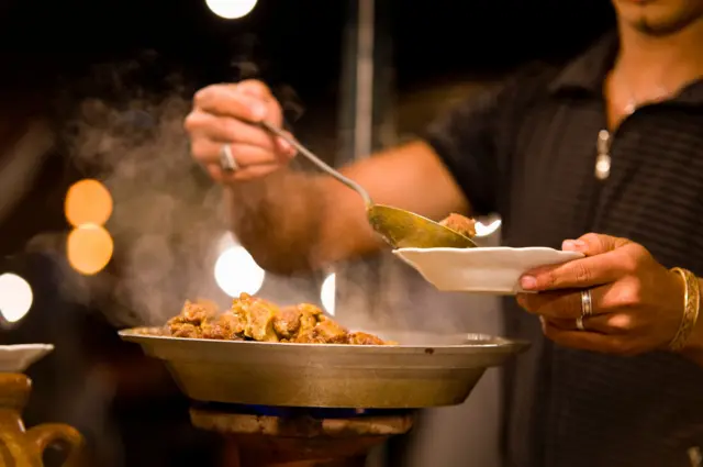 شخص يسكب اللحم من مقلاة على موقد صغير بدائي