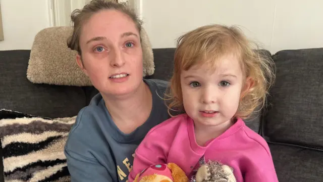 Una foto de Emily y su hija. Ella lleva un jersey gris y su hija, uno rosa.