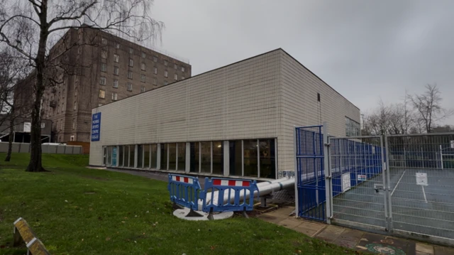 Exterior del edificio de la piscina, un edificio rectangular con ventanas de vidrio y un cartel azul.
