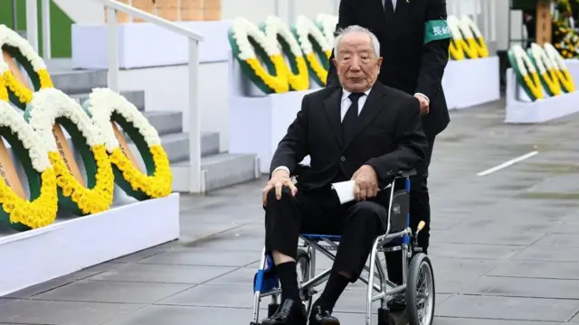 黒い喪服姿で車いすにのる白髪の西岡さんを、係員が案内している