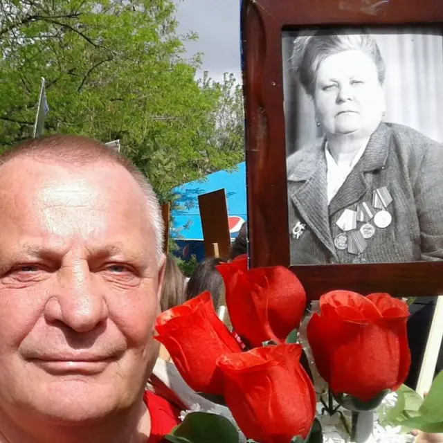 Літній чоловік на фоні квітів і чорно-білого портрету своєї матері
