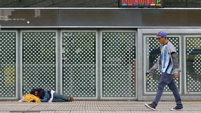 Un hombre pasa frente a la estación de metro Constitución, en Buenos Aires, mientras una persona duerme en el suelo.