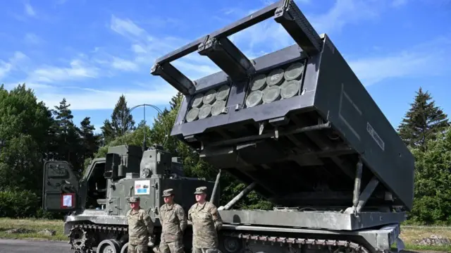 İngiliz Ordusu'na bağlı 1. Royal Horse Artillery birliğinin askerleri, 20 Temmuz 2022 tarihinde Almanya'nın güneyindeki Eschenbach yakınlarında bulunan Grafenwöhr'de düzenlenen "Dynamic Front 22" tatbikatı sırasında, zırhlı ve kendinden tahrikli bir M270 Çok Namlulu Roketatar Sistemi (MLRS) önünde duruyor.