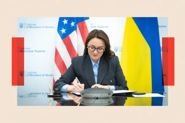 Свириденко за столом підписує документ, за нею - прапори України та США