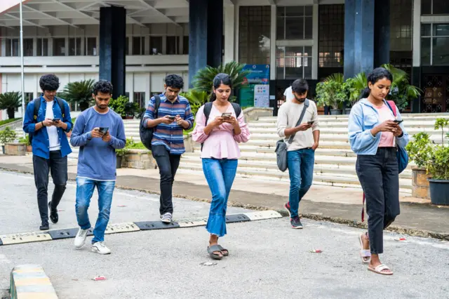 විශ්වවිද්යාල පරිශ්රයක ජංගම දුරකථනය භාවිතා කරමින් කාර්යබහුලව සිටින සිසුන් පිරිසක්