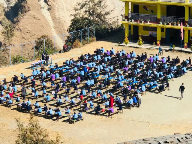 म्याग्दीको फलियागाउँस्थित धनजनता माध्यमिक विद्यालयका विद्यार्थीहरू कक्षाकोठाबाहिर बसेर आन्तरिक परीक्षा दिँदै