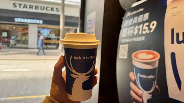 手中举着一杯瑞幸咖啡。