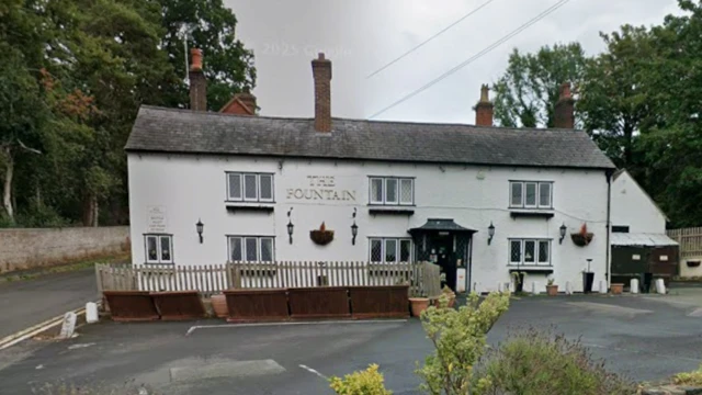 El pub es un edificio blanco de dos niveles con un estacionamiento frente a él y algunos asientos al aire libre.