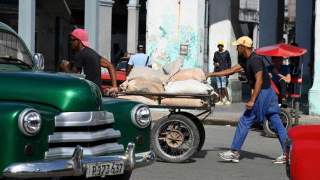 Pessoas passando no centro de Havana em meio a carros
