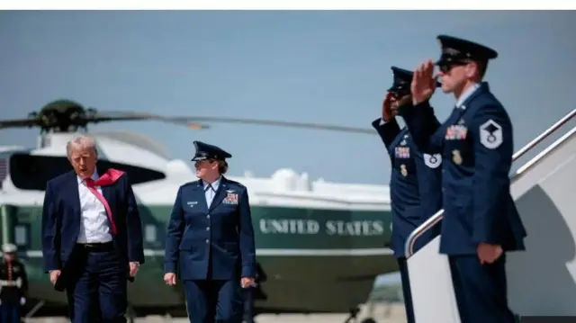 Aarẹ Donald Trump lẹgbẹẹ oyinbo ologun obinrin kan, awọn ologun meji n bẹri fun wọn. Baaluu ilẹ America kan wa lẹyin ninu aworan naa.