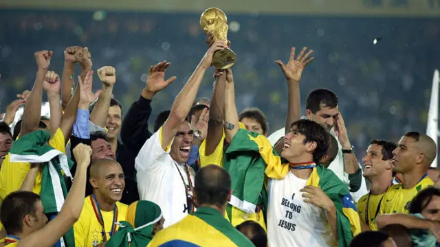 A brazil focista, Kaká, a 2002-es világbajnokságon egy „I belong to Jesus” (Jézushoz tartozom) feliratú pólóban, a csapattársaival körülvéve ünnepel. 