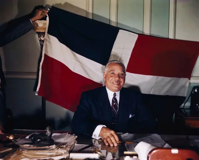 Rafael Leonidas Trujillo con la bandera de República Dominicana en el fondo