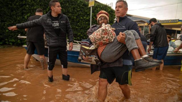 Homem carrega mulher no colo durante enchente no Sul
