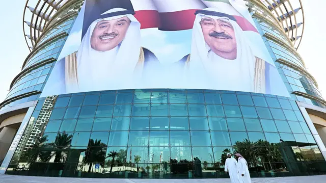 Ciudadanos kuwaitíes pasan frente a grandes retratos del emir de Kuwait, el jeque Mishal al Áhmad al Yáber al Sabah, y del príncipe heredero, el jeque Sabah al Jalid al Sabah, exhibidos en la fachada del Instituto de Diabetes Dasman en Ciudad de Kuwait el 10 de marzo de 2026.