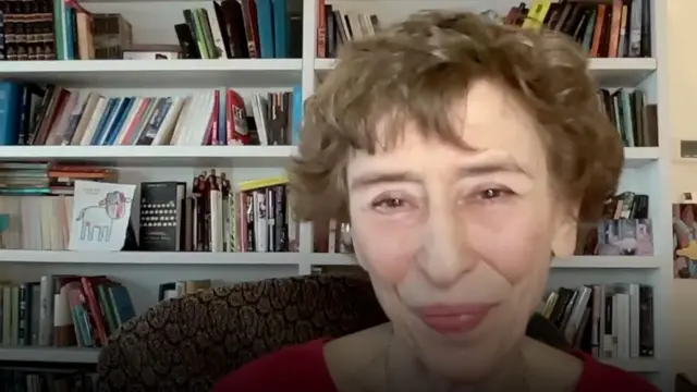 Женщина с короткой стрижкой улыбается на фоне книжных полок