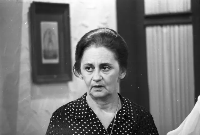 Laura Cardoso atuando, em cena dentro de casa, com olhar sério