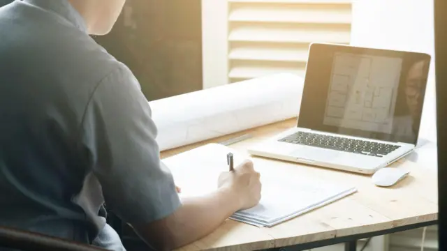 una mujer sentada en un escritorio escribe en una libreta 