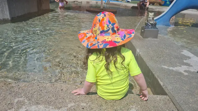 Criança com roupa de banho amarelo neon e chapéu, à beira de uma piscina